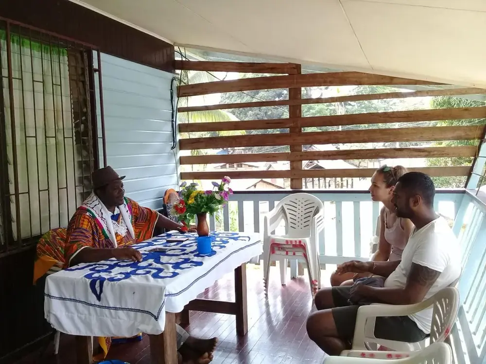 Gastheer Don Adjako spreekt met bezoekers op de veranda